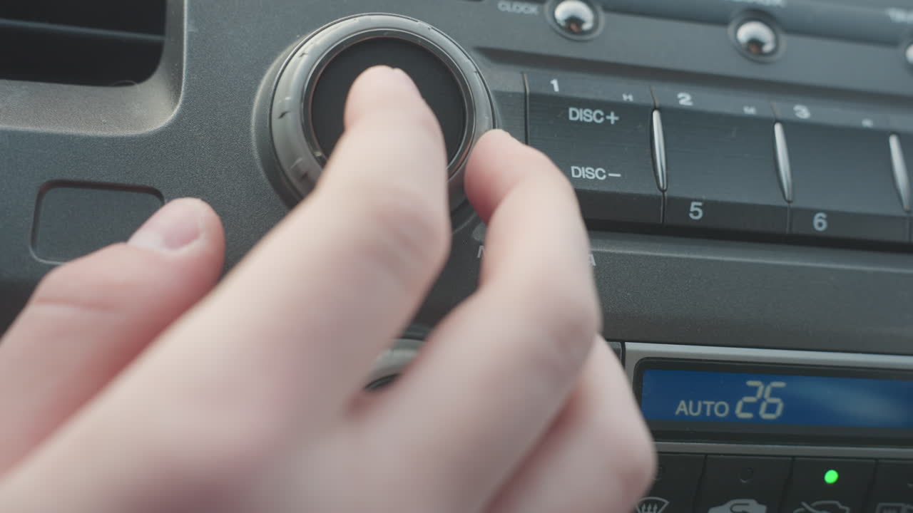Close up hand turning volume knob then pressing power button on car audio control panel capturing finger interaction with smooth rotary dial and media interface in modern vehicle interior