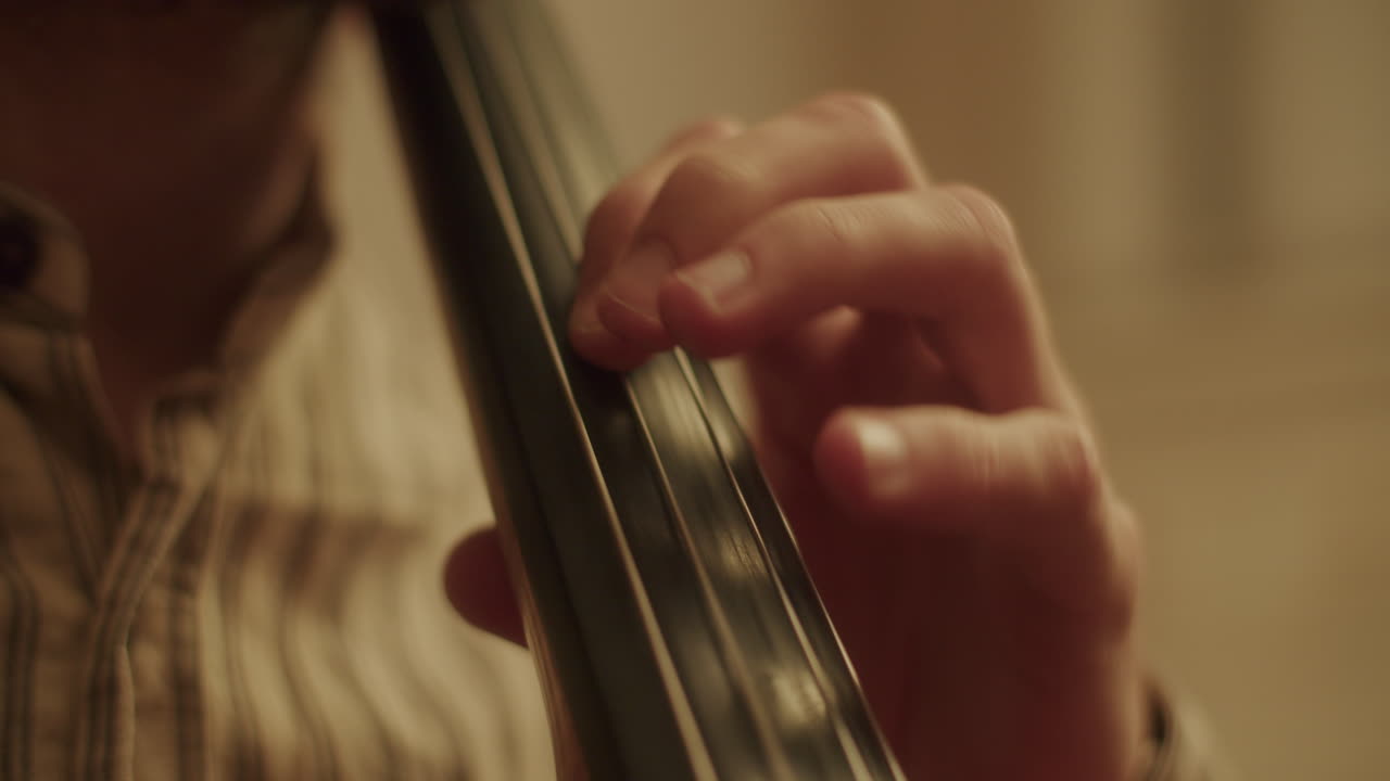 Close up shot of the left hand of a cellist moving over the strings of a cello, doing vibrato with the hands