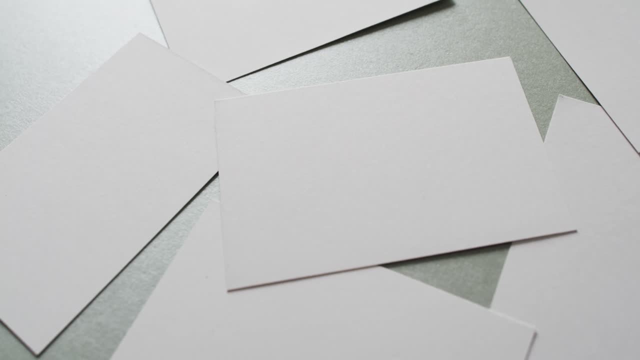 Close up of white business cards scattered on grey background, copy space, slow motion