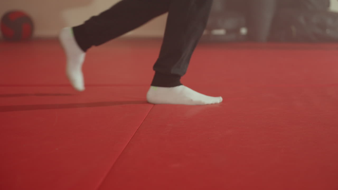 Closeup view of athlete foot in black sock on red martial arts mat with long shadow stretching across floor inside training gym symbolizing motion, balance, energy, focus, during workout session