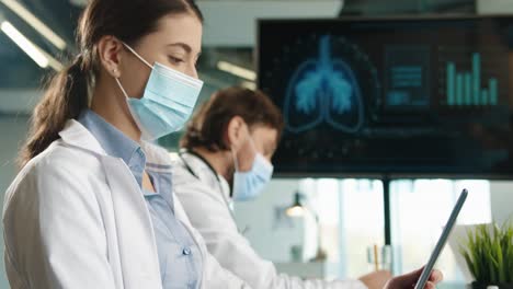 close-up view of caucasian female doctor typing on tablet and looking at digital screen presentation sitting at meeting with multiethnic doctors group