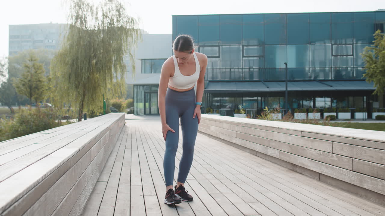 Sportliche Läuferin in Sportbekleidung mit Muskelschmerzen nach dem Joggen im städtischen Stadtpark an einem sonnigen Tag