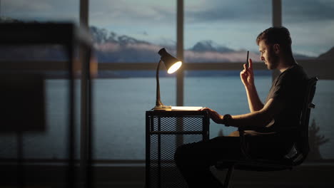 serious concentrated young male student studying at home office sitting in cozy workplace at night under lamplight. a young man thinks creates a creative project and writes it down with a pen.