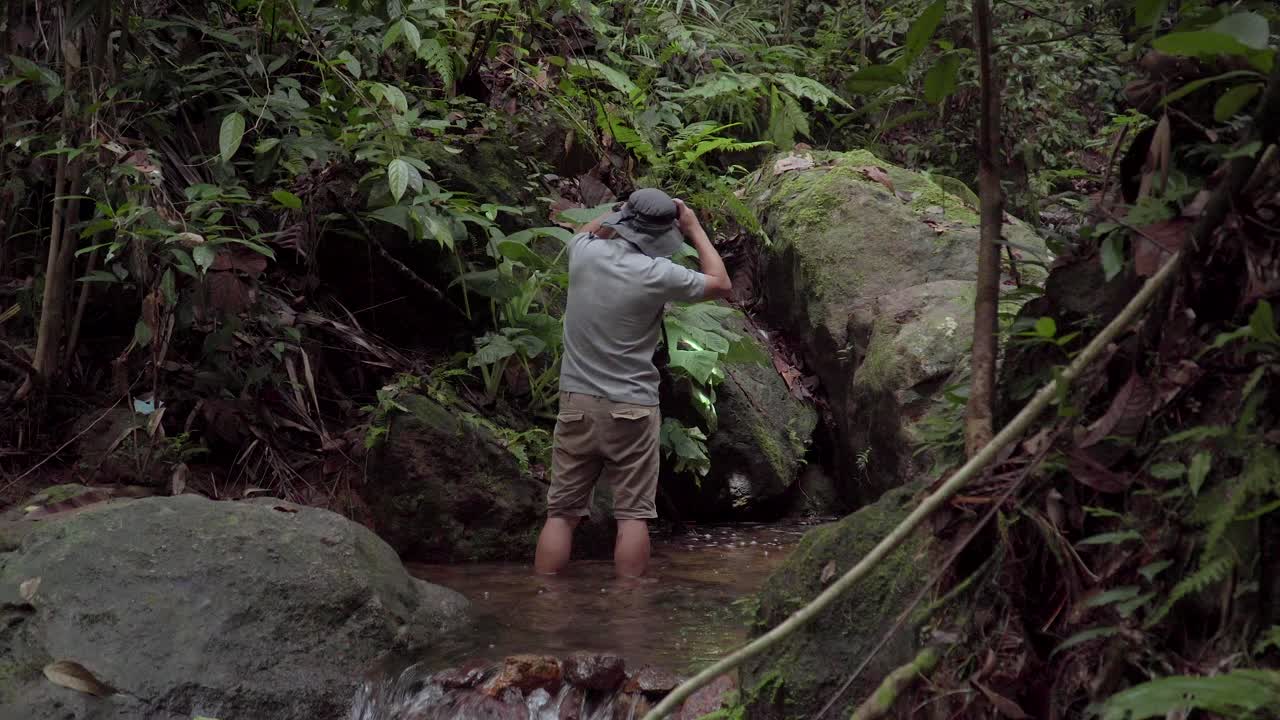 정글, 숲 또는 열대우림에서 하이킹 헤드라이트를 사용하여 탐험과 발견을 둘러보고 있는 강, 개울, 개울에 서 있는 남성 여행자 하이커