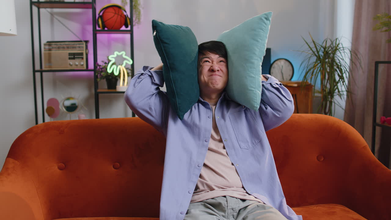 Repair work at neighbours concept irritated man at home cover ears with pillows annoyed by noise