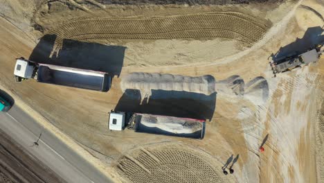 aerial view on tipper truck is unloading gravel from trailer over construction site for new traffic roundabout
