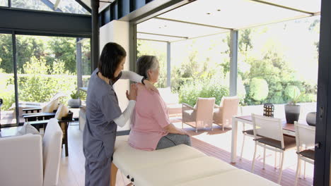 providing physical therapy, therapist massaging senior woman's shoulder at home
