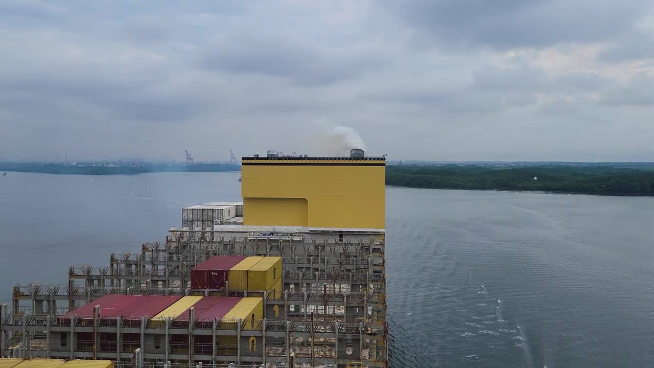 An aerial view captures steam and exhaust from the funnel of a massive container ship, highlighting the power and environmental impact of maritime shipping in the Panama Canal.