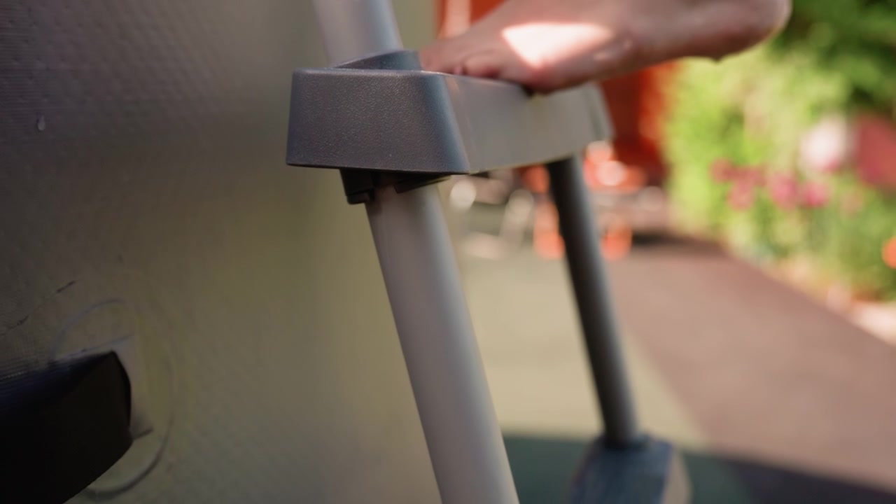 Bare foot ascends gray plastic ladder focusing on step and leg movement. background is softly blurred with hints of outdoor setting featuring greenery and warm tones. Lighting creates soft