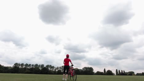 caucasian female cyclist in red top walking with her bike in a park in slow motion