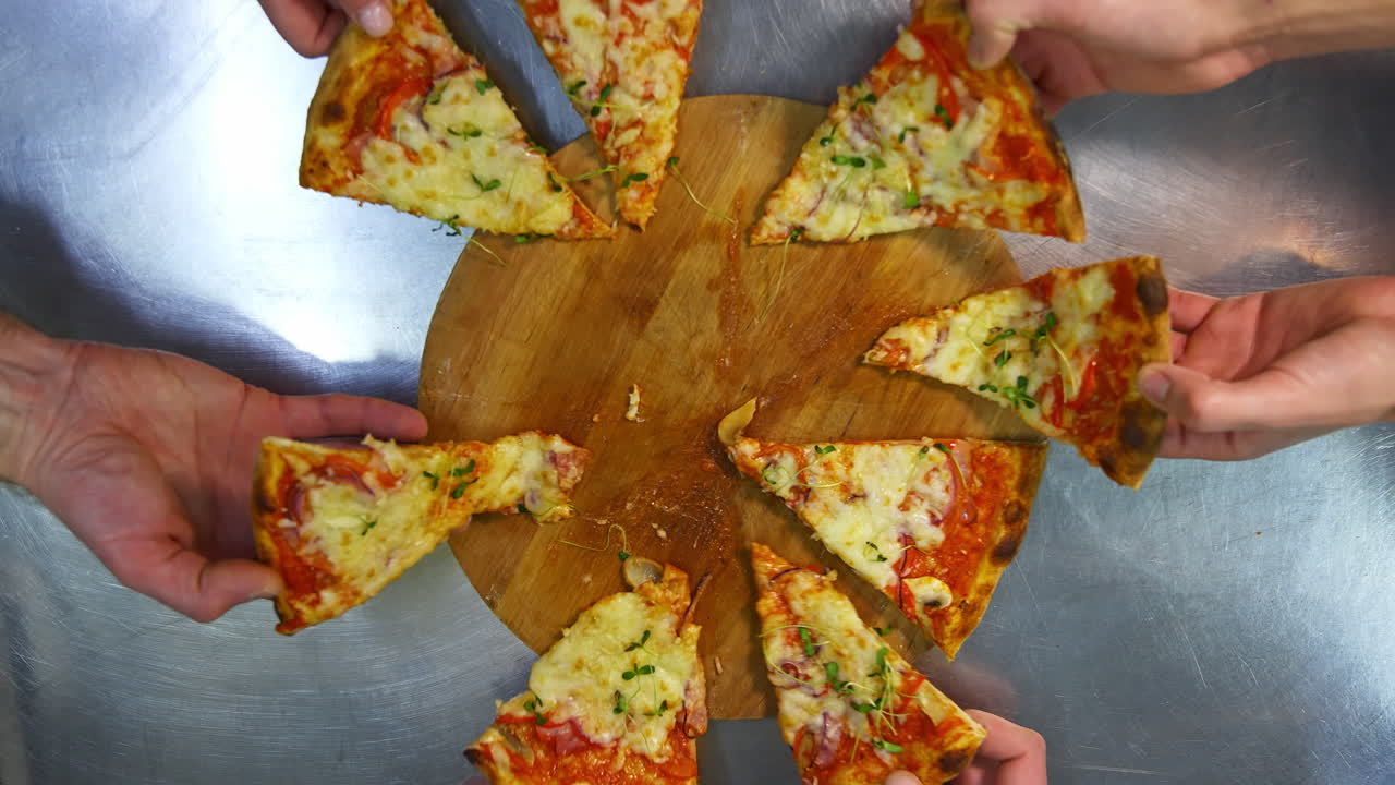 Hands are taking pizza portions. Ready pizza on the table. People take slices of delicious pizza in pizzeria. Top view.