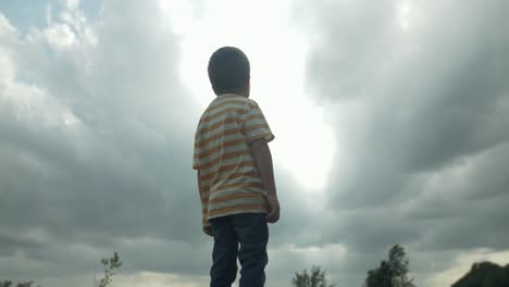 a young boy standing outside in sunlight. looking up at the sky in slow motion, his eyes full of wonder and curiosity watching clouds. this captures the innocence and imagination of childhood.