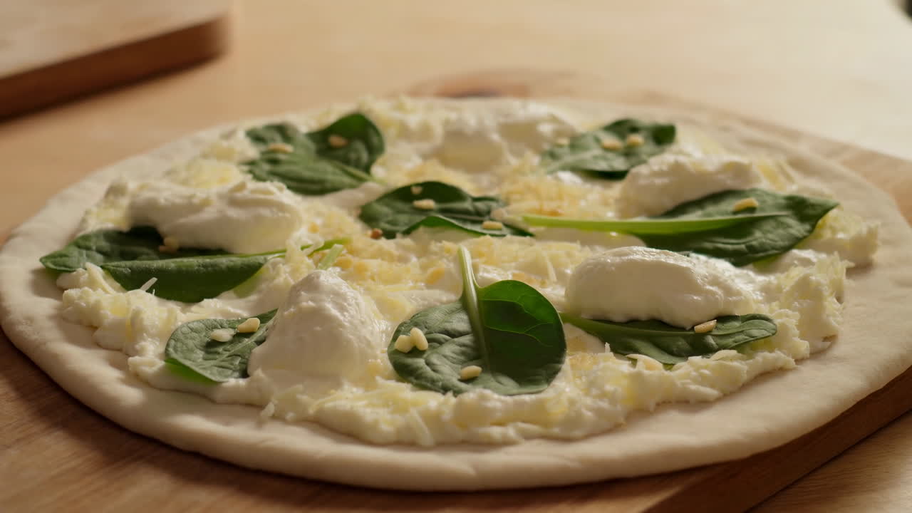Pizza cruda con ricotta e spinaci su pala di legno, cucchiaiate cremose di ricotta fresca, foglie di spinacini
