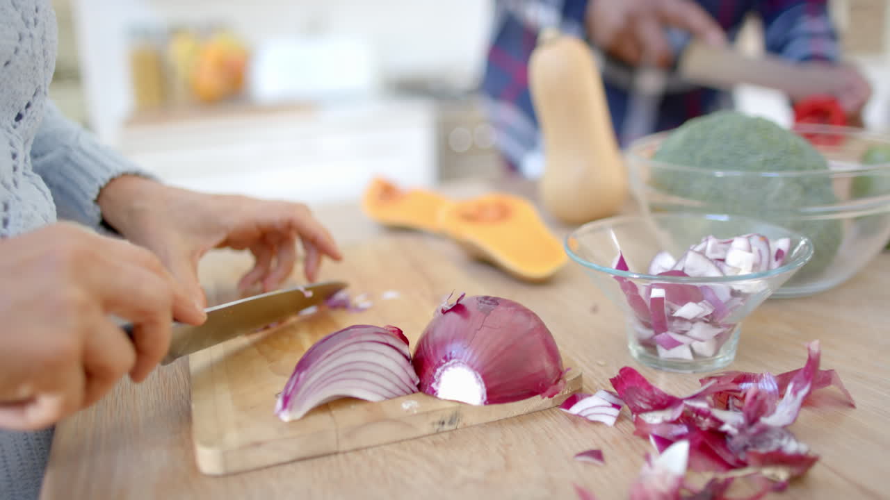 Midsection of senior diverse couple cooking, cutting vegetables in kitchen, slow motion