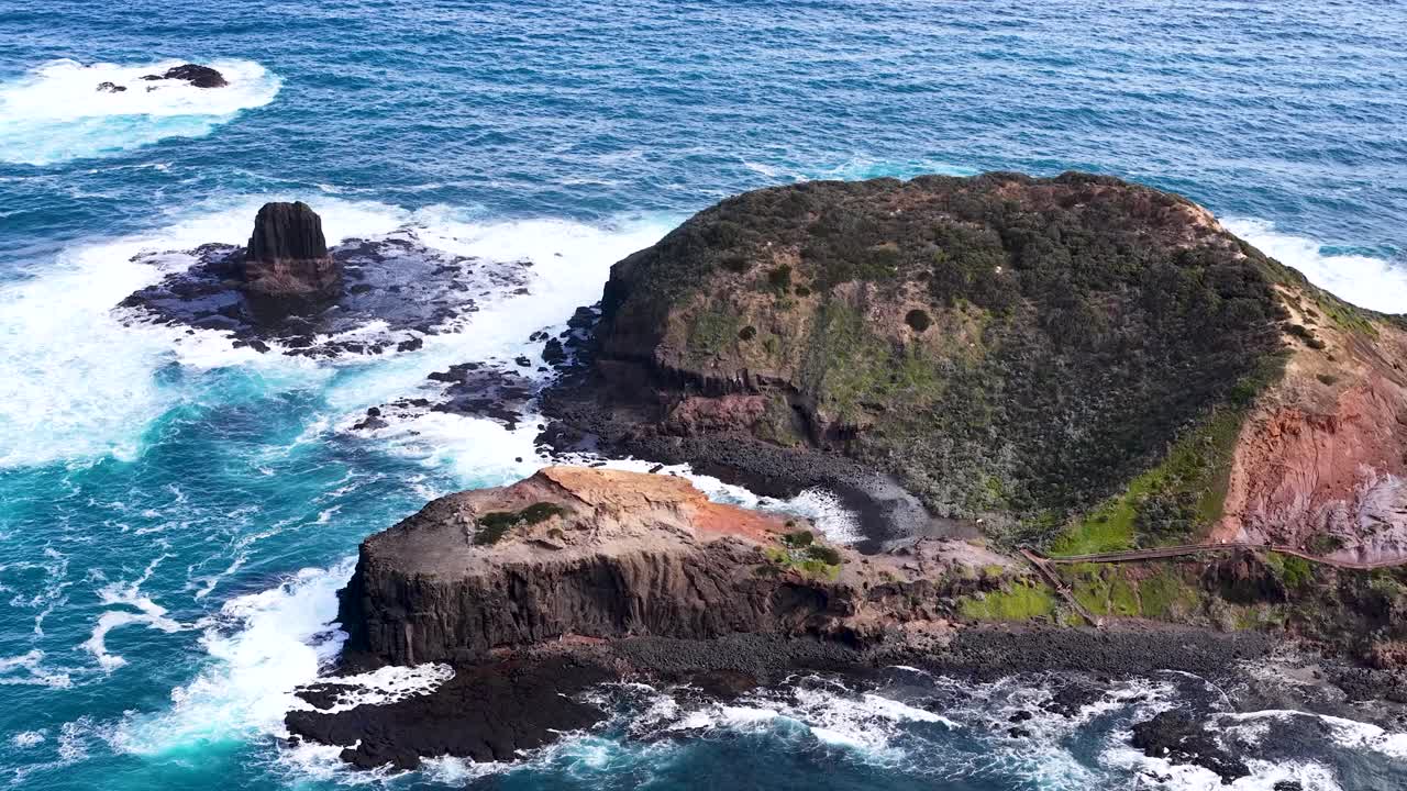 Drone camera glides above rugged island, turquoise ocean waves, and dramatic coastal cliffs in daylight