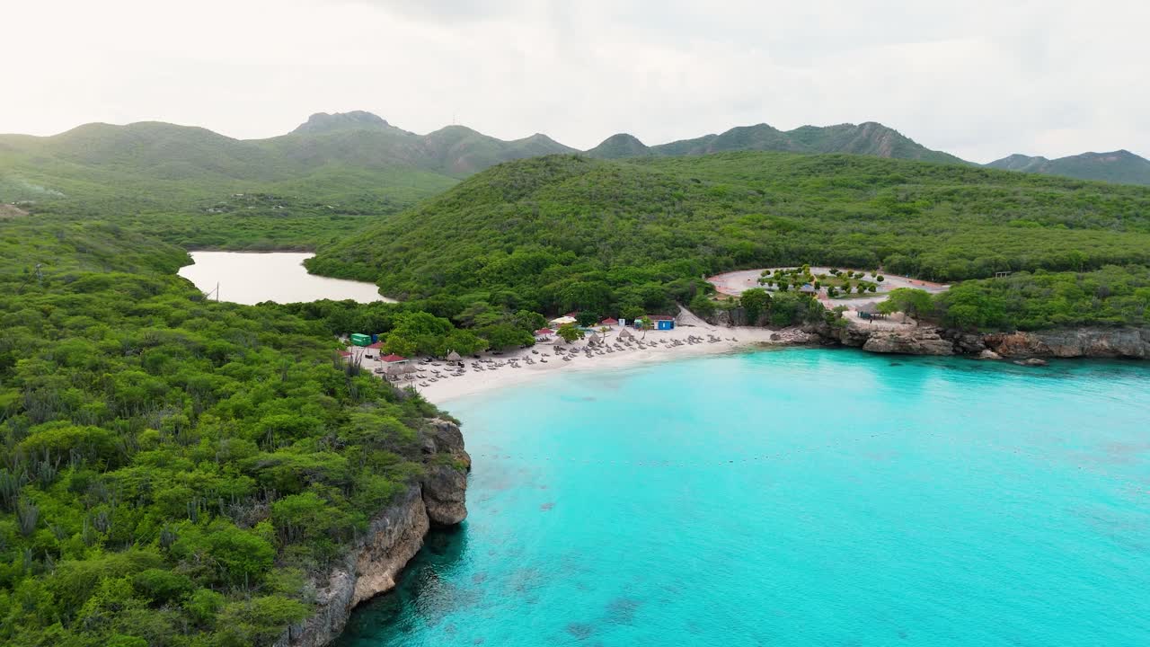 Drone panoramic overview of the coastline at Kenepa Grande , Curacao, with clear turquoise waters, lush green surroundings, and sandy beach shoreline