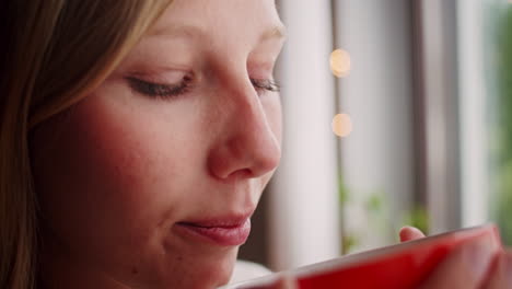 mujer rubia con ojos azules tomando café en la ventana de casa, cerrada
