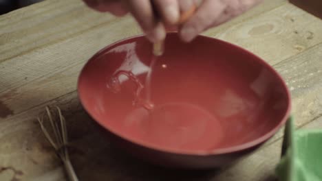 cracking an egg into a red bowl ready for mixing