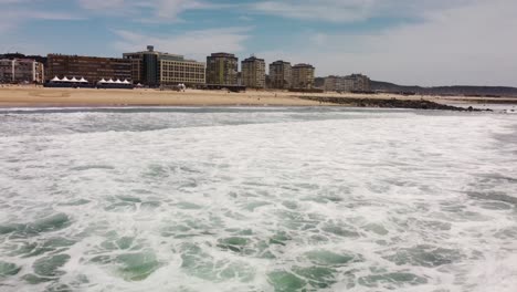 flyover ocean waves and seafoam towards to costa da caparica coastline, tilt up shot