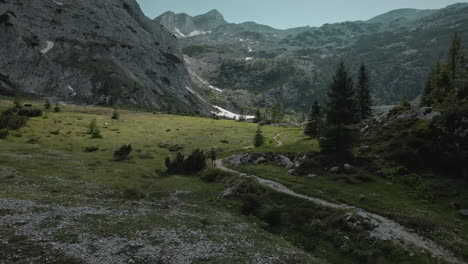 Drone-shot-of-the-valley-and-mountains-in-the-back,-a-small-path-in-the-middle-of-the-valley-a-hiker-is-walking-on,-clear-blue-sky