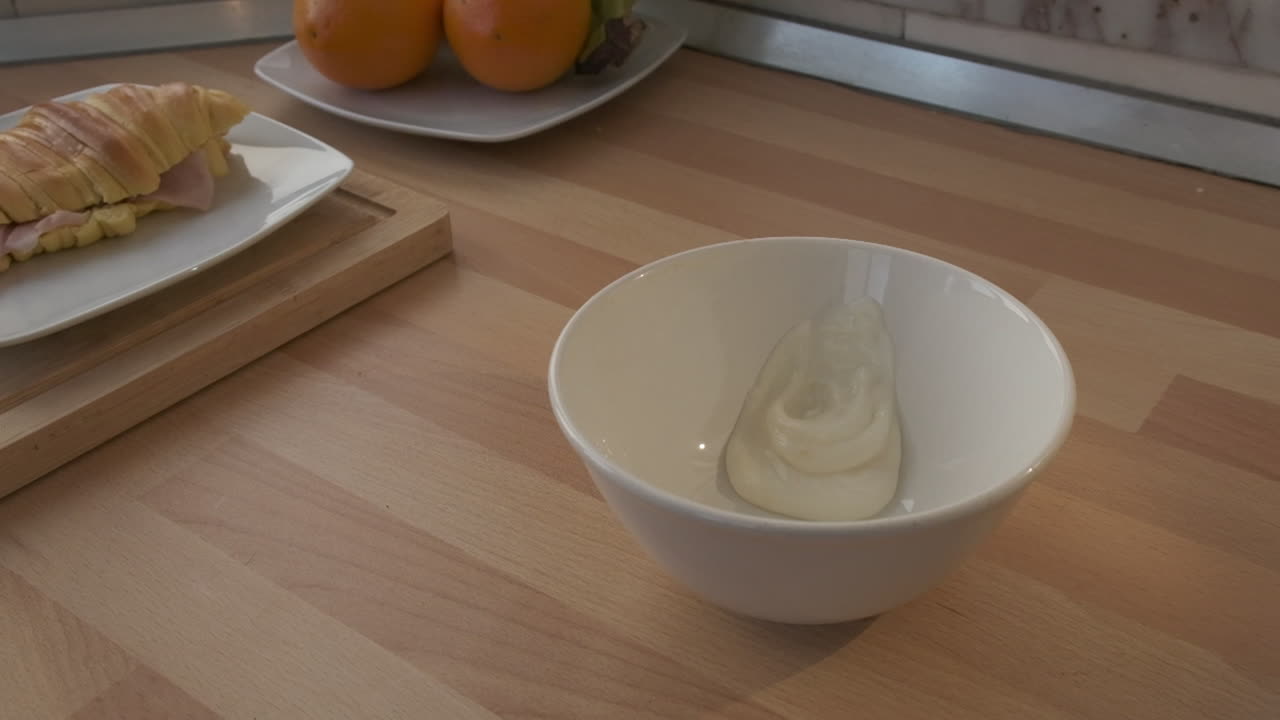 Yogurt che cade in una ciotola - Croissant con prosciutto in un piatto a lato - slow motion