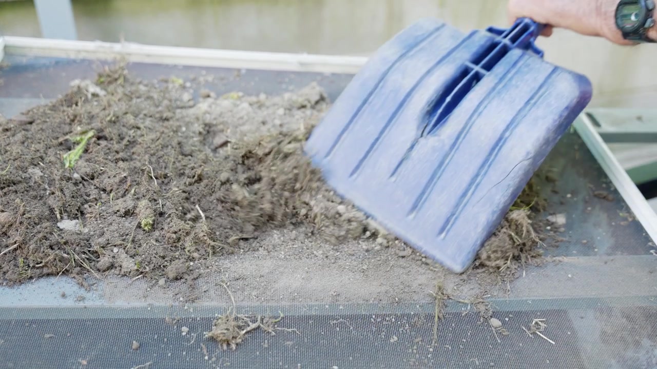 Close-up of a gardener's hands sieving fresh soil through a mesh screen to remove debris