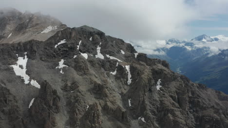 Flying-over-mountain-top-with-thawing-snow-on-rocks