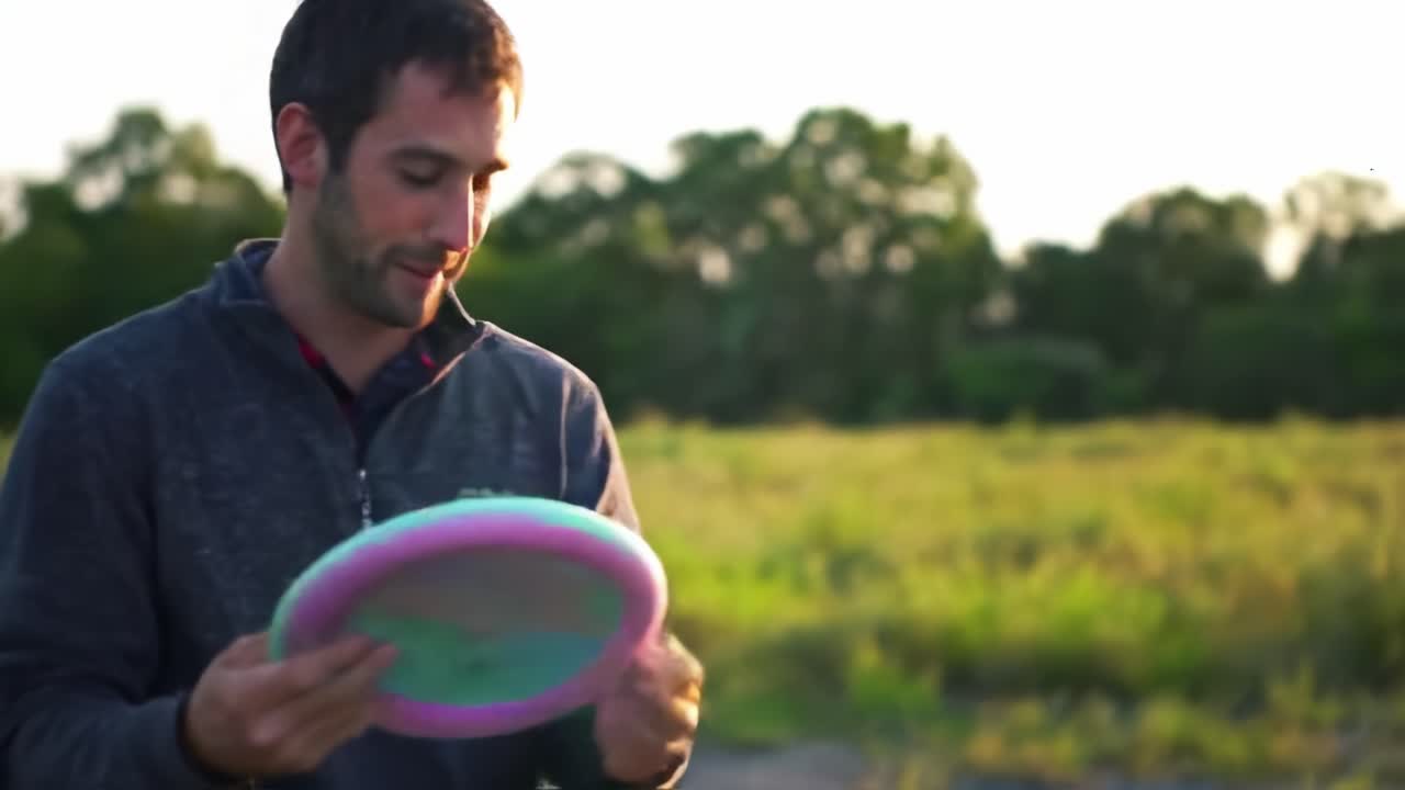 A Joyful Moment of Playtime: A Man Engaging with His Happy Dog While Playing Fetch with a Colorful Disc in a Lush Green Field Under the Setting Sun