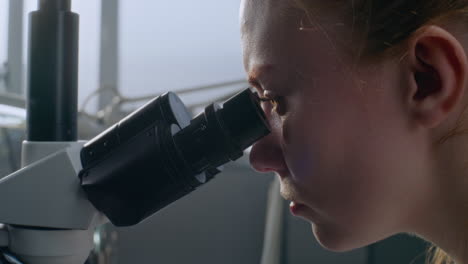 mujer mirando a través del microscopio
