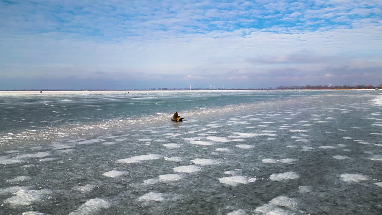 hombre pescando en un lago congelado, lago st clair, bahía de mitchell, toma aérea de drones de 60 fps, con textura de lago helado y fondo de molino de viento