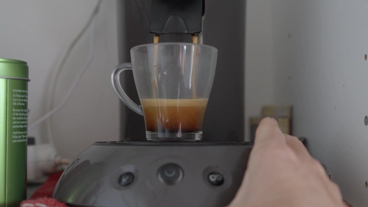 Bir makineden cam bardağa dökülen taze kahve. Modern bir mutfak ortamında krema ve buharla espresso çekiminin yakın çekimi.
