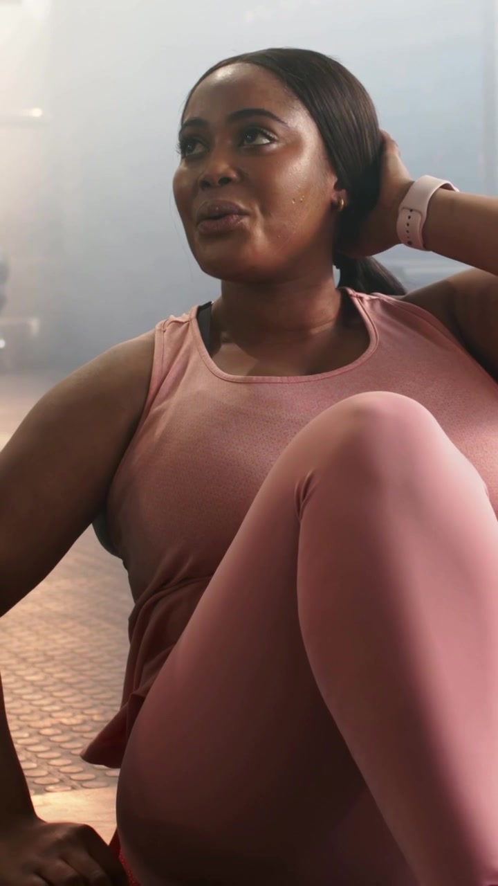 Vertical video: Crunching woman in pink on gym mat after tucking hair, checking watch for health