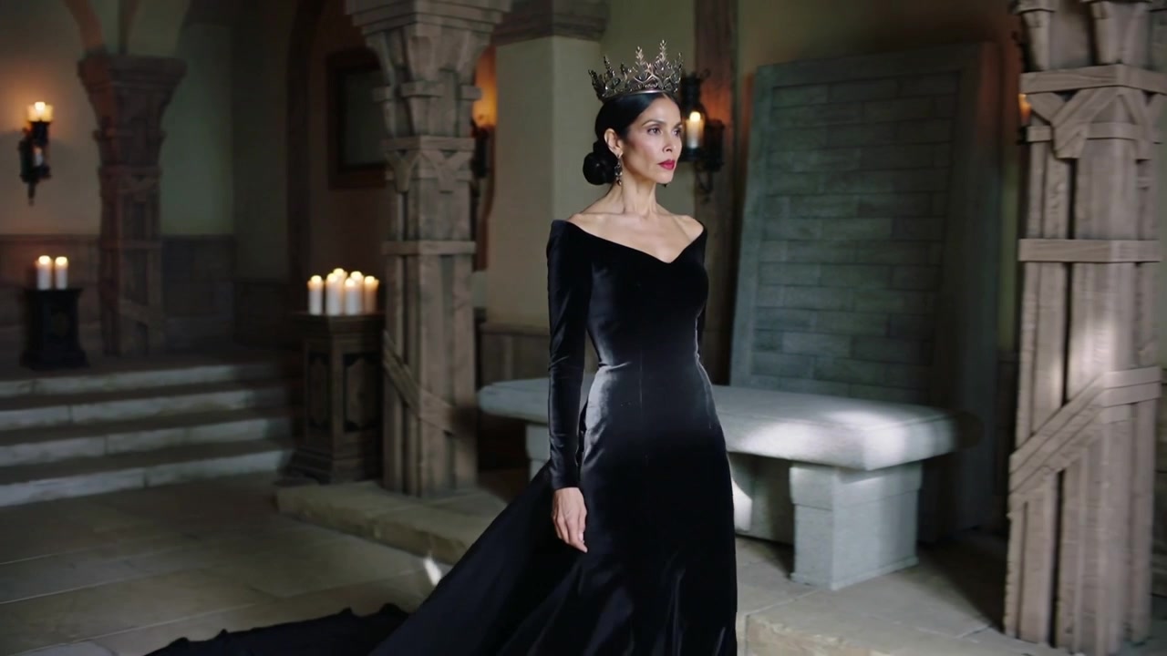 Donna incoronata che cammina in un lungo abito nero, scendendo gradini di pietra per una cerimonia in una grande sala, con candele.