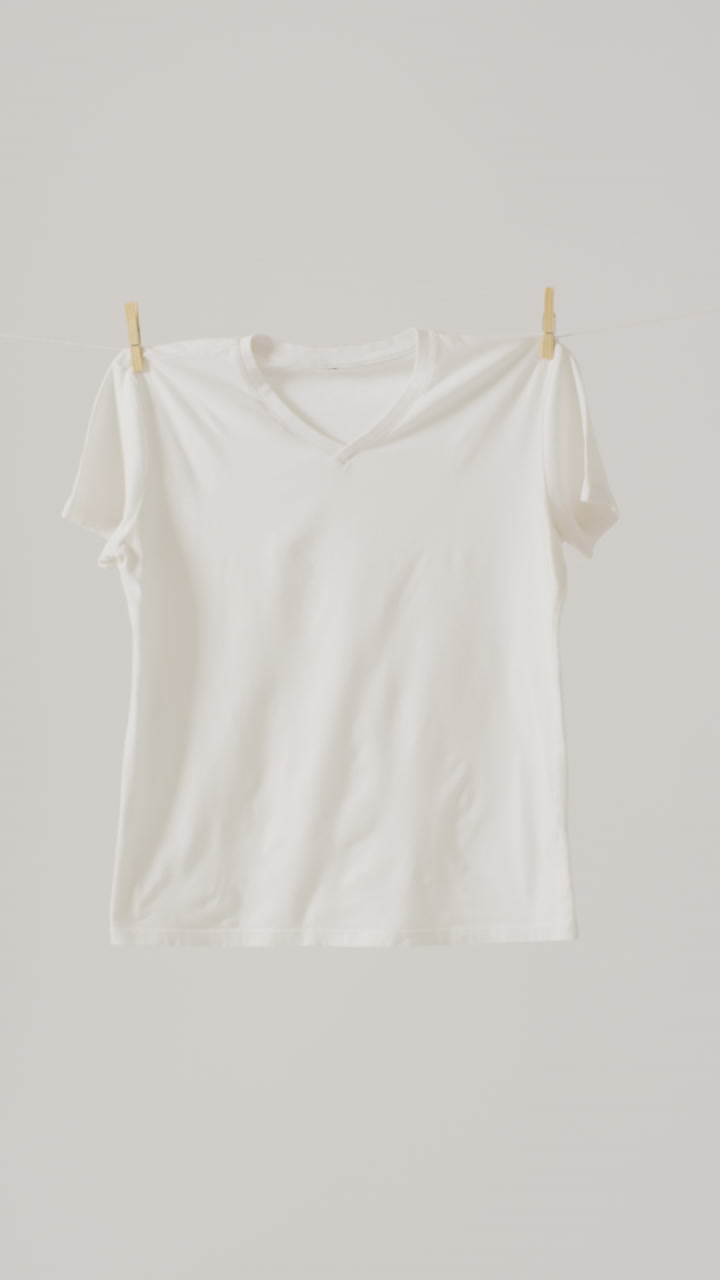 Vertical video of close up of white t shirt hanging on white background with copy space