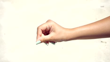 close up of woman pouring sand running through fingers at the beach with sun flare