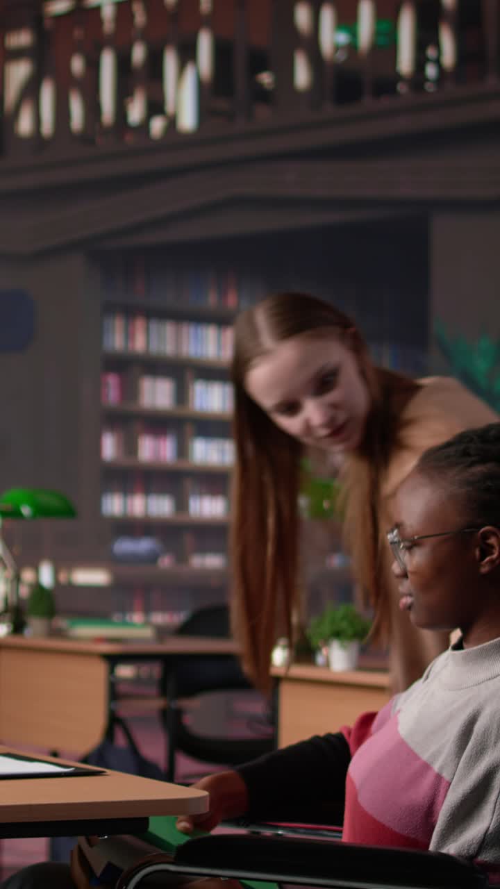 Vertical video girl pushing her colleague with physical impairment through the library