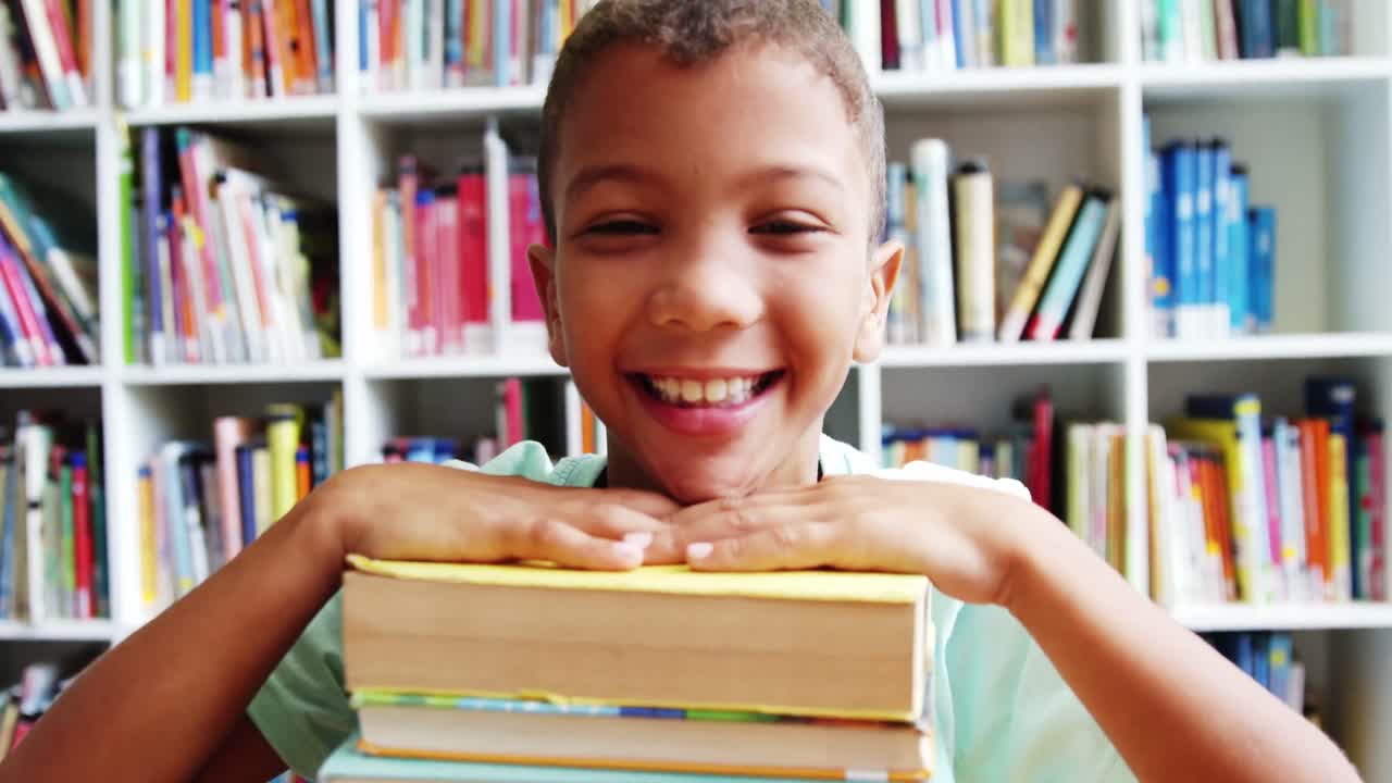 retrato de un niño sonriente apoyado en una pila de libros en el aula