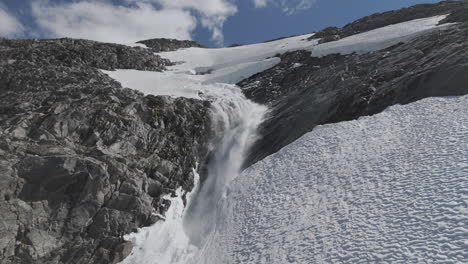 slowmotion drone shot flying around a powerfull waterfall near langvatnet lake in norway close to the strynefjellsveg breaking through ice and snow on a sunny day surrounded by shiny rocks log