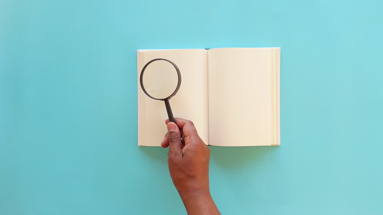 una mano sostiene una lupa sobre un libro abierto