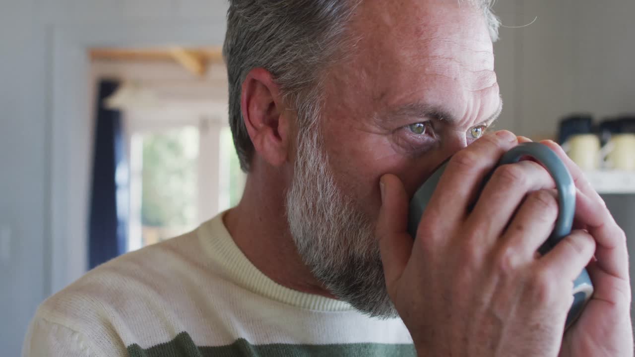 hombre caucásico maduro mirando por la ventana y bebiendo café
