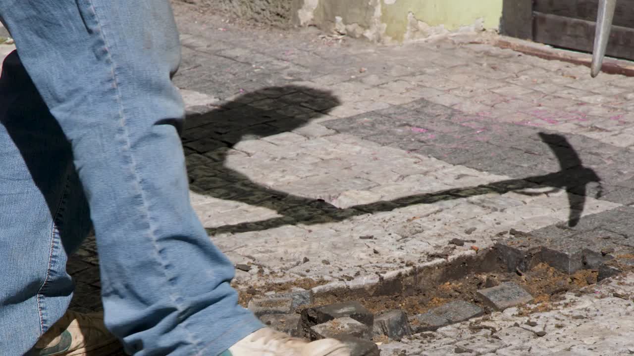Veduta a livello del suolo di un operaio che usa un piccone per rimuovere pietre da un marciapiede.