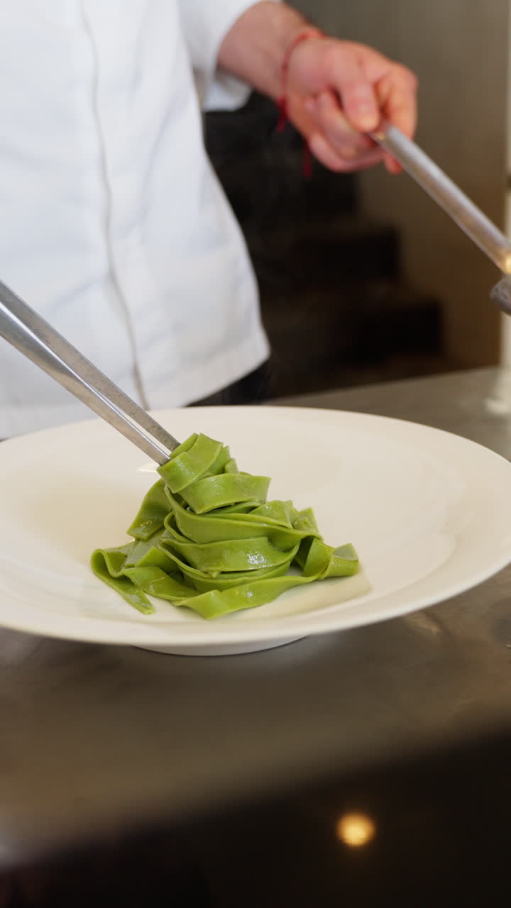 Chef Plating Fresh Green Pasta with Tongs and Ladle in a Professional Kitchen