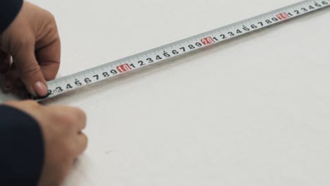 primer plano de manos femeninas midiendo con un lápiz sobre tela blanca usando una regla en una fábrica textil
