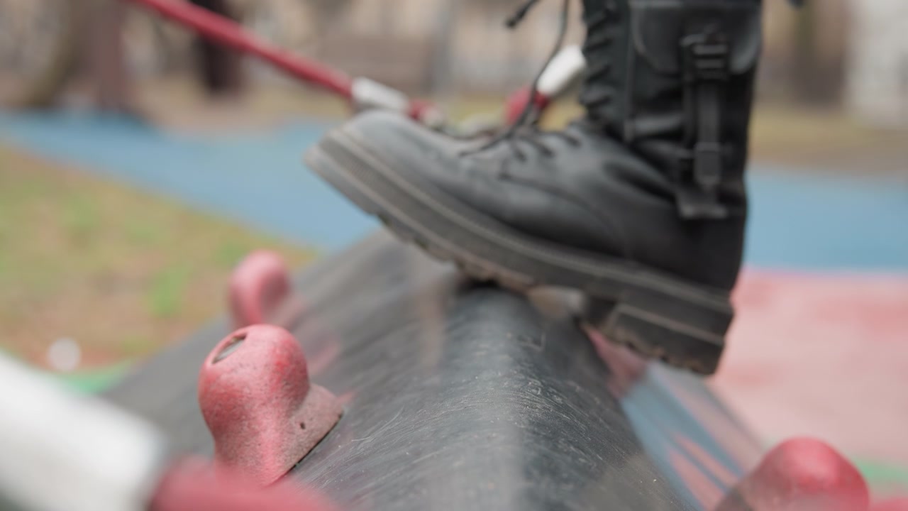 Boots striding curved pipe with attitude, confident punk performer balancing on textured tube secured by red rope anchors, bold scuffed leather and heavy sole hitting surface, urban alley backdrop