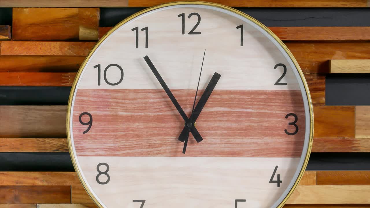 Zoom in close up time-lapse of wood wall clock approaching one o' clock themes of deadline appointment late departure on a wooden background.