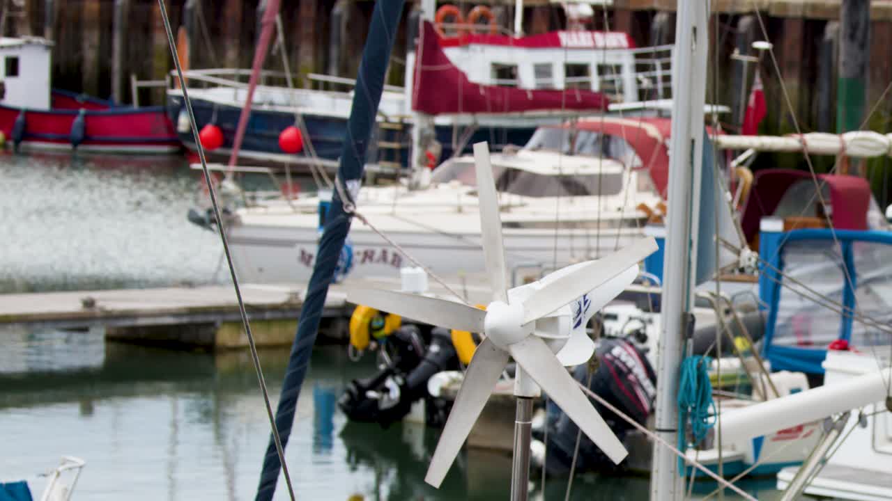 Small wind turbine rotates on docked sailboat, overcast daylight, steady camera, marina background