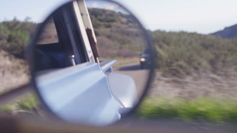 closeup of the rear view mirror of an old pickup truck as it drives through a rural area