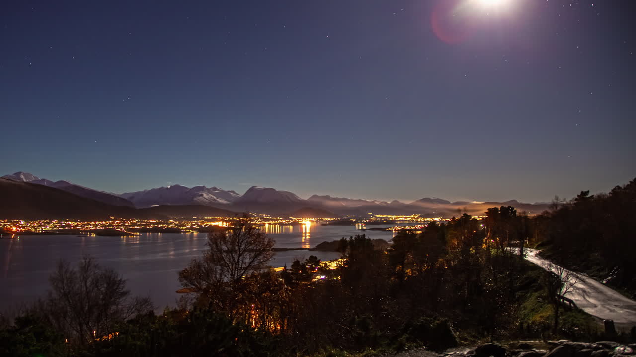 Timelapse de la ciudad noruega de Aalesund iluminada por la noche bajo un cielo estrellado y una luna resplandeciente