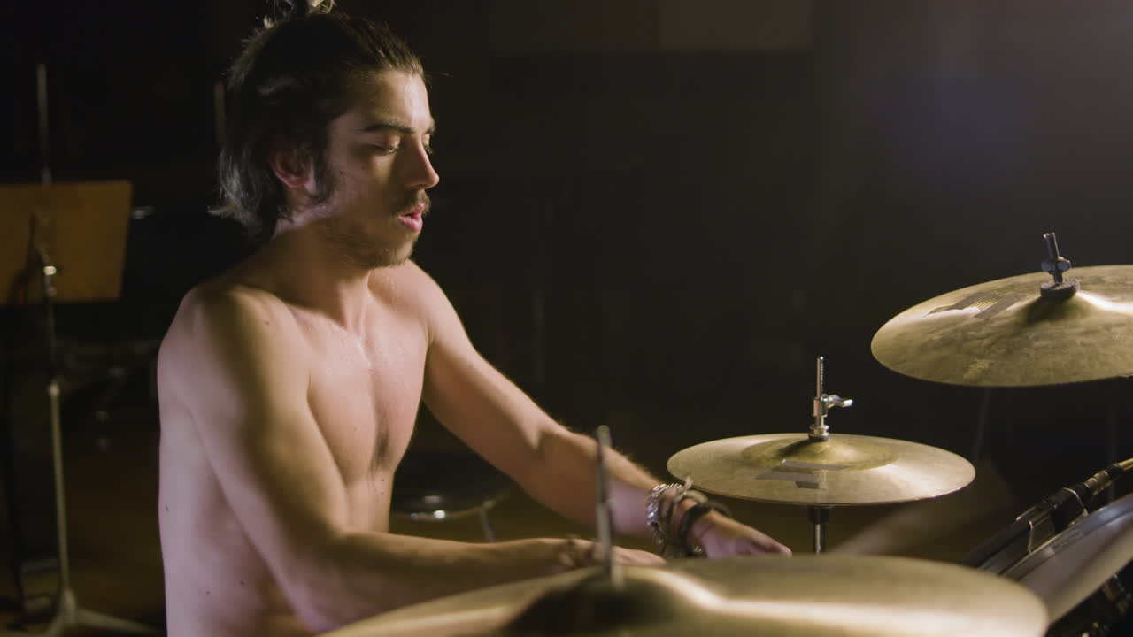 baterista masculino sin camisa enérgico con barba tocando la batería