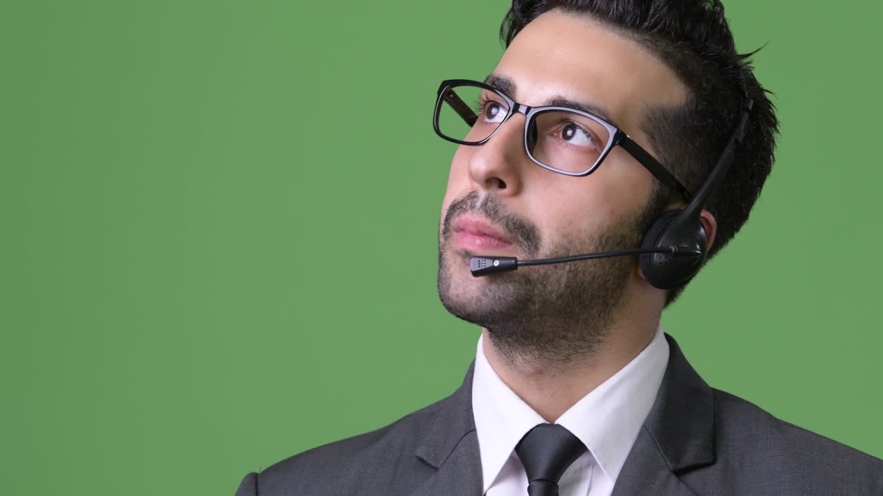 Young handsome bearded Persian businessman against green background